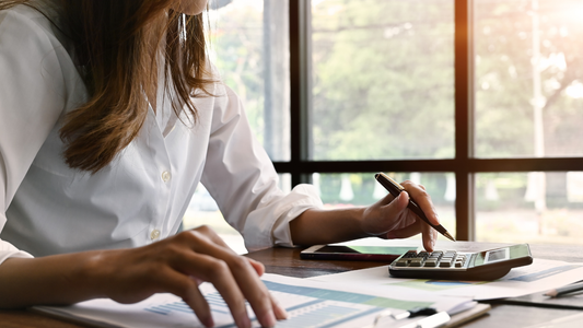 A person sitting at a desk using a laptop and calculator, reviewing financial documents and making calculations.