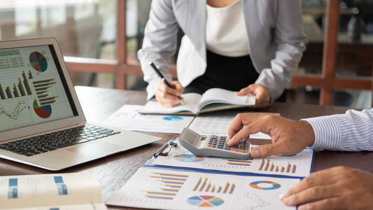Two people sitting at a table with a laptop and papers showing charts and graphs.