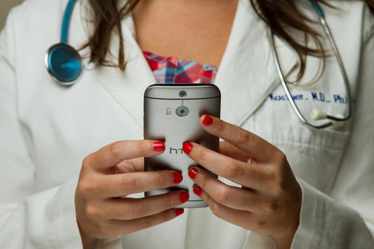 Female doctor in a white coat with a stethoscope holding a smartphone, symbolizing digital health startups pitching key metrics to VCs